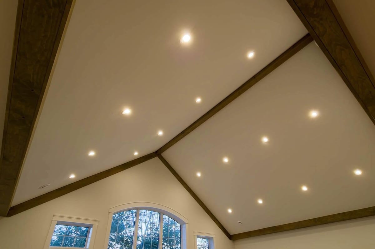 A vaulted ceiling with recessed lighting laid out along the beam lines.